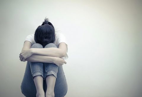 A women sits with her legs bent and her head between her knees.